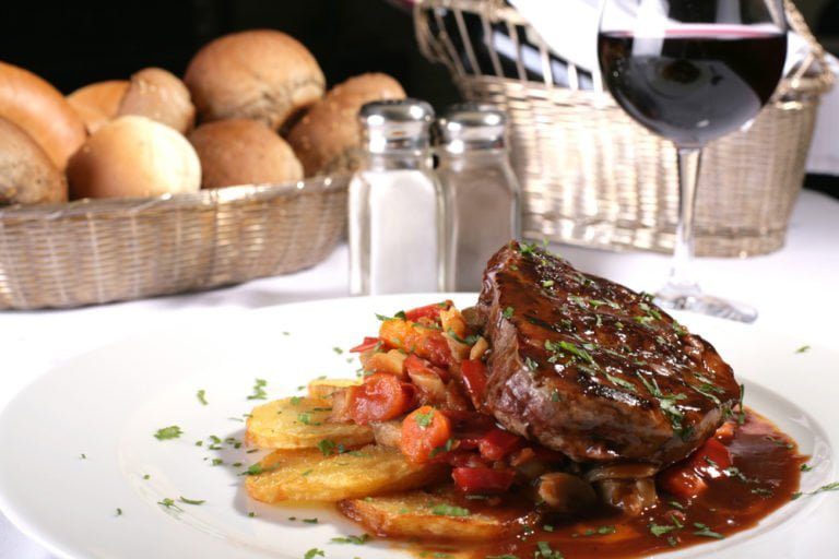 A fancy steak dinner with a glass of wine and bread rolls