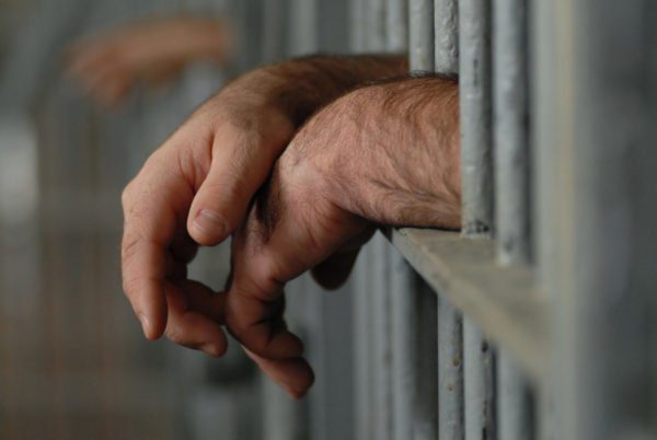 Manos de hombre atravesando los barrotes de la prisión
