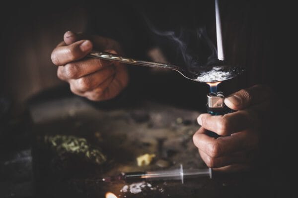 A person uses a lighter to heat up drugs in a spoon.