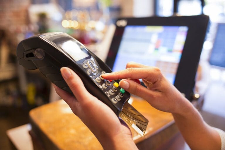 A woman's hand holding a credit card in a billing terminal to illustrate return fraud laws in california